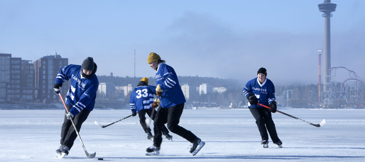 Neljä ihmistä pelaamassa jääkiekkoa Näsijärven jäällä. Taustalla Näsinneula.