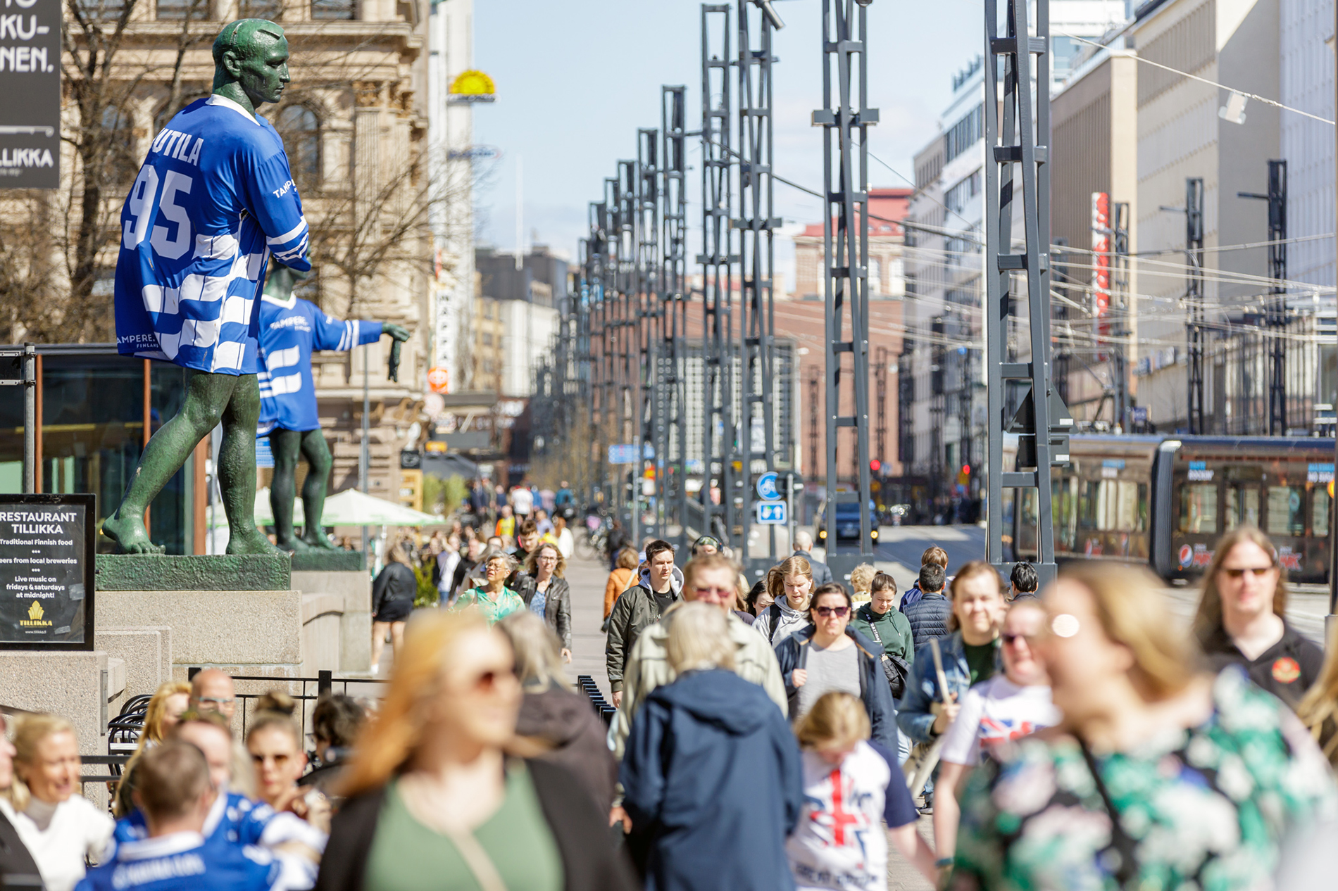 Hämeensilta bridge's statues wearing blue jerseys. People walking down the bridge.