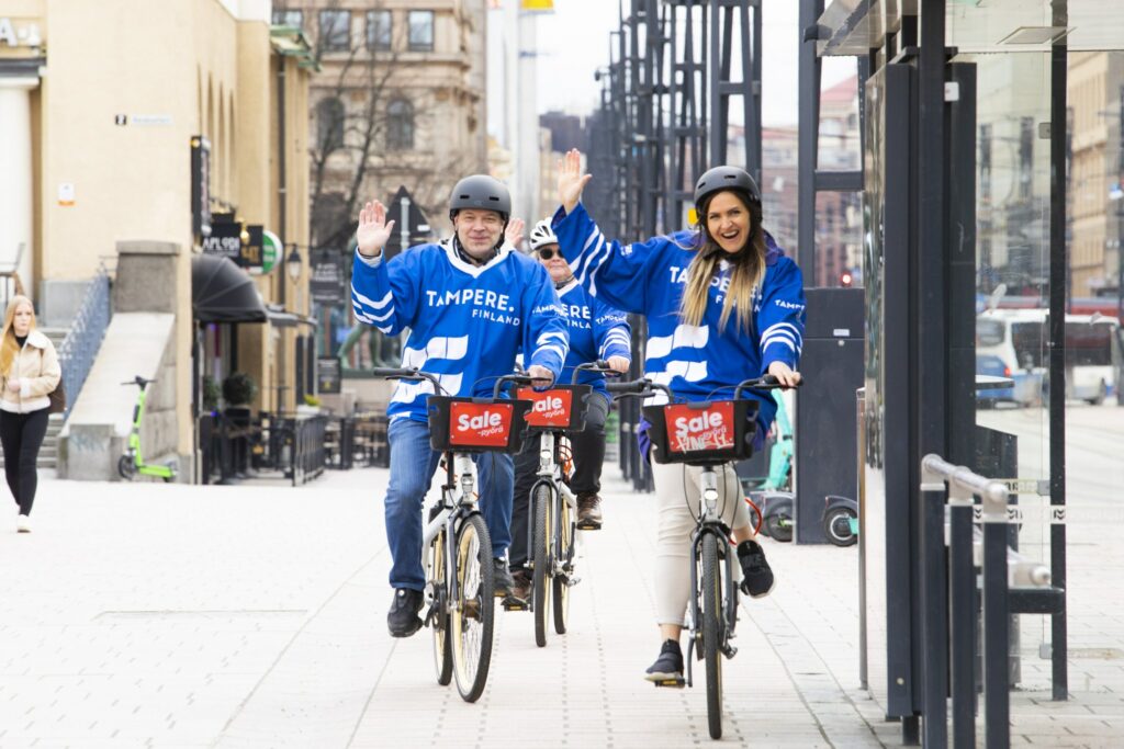 Kolme henkilöä ajaa kaupunkipyörillään Tampereen pelipaidat yllään.