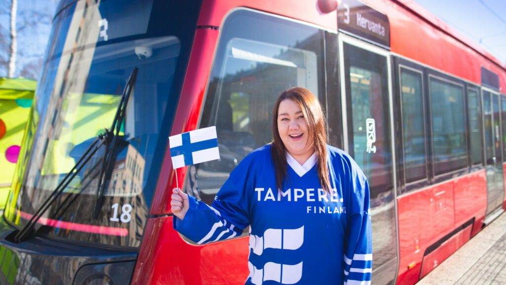 A person waving a Finnish flag next to a tram.