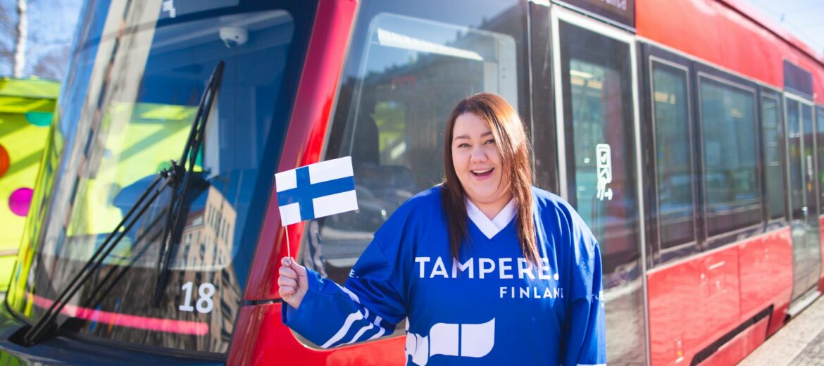 A person waving a Finnish flag next to a tram.