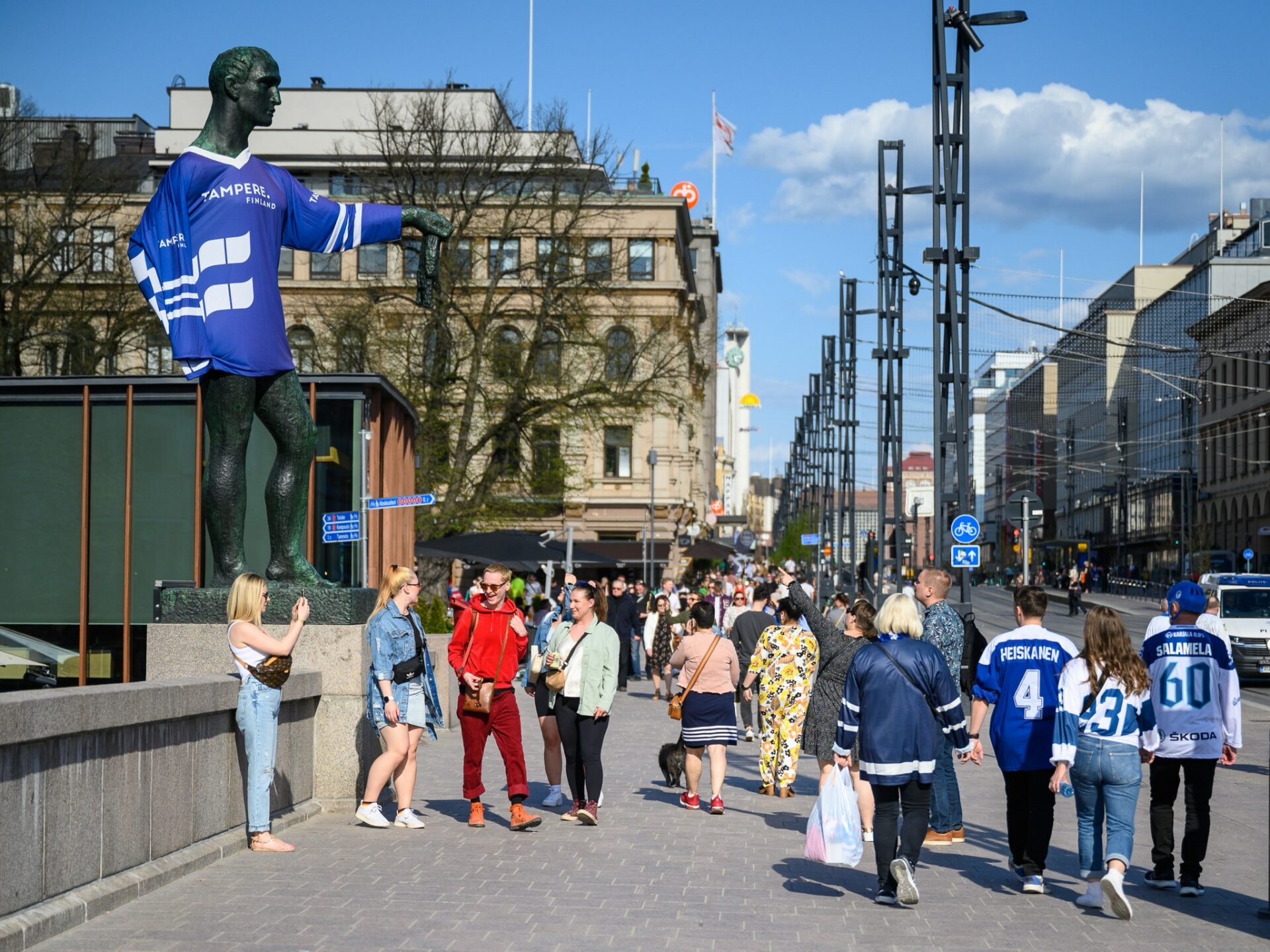 People walking down the Hämeensilta bridge. Pirkkalais statue is dressed with a blue jersey.