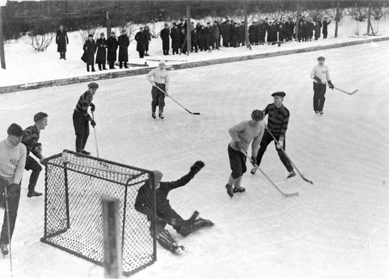 Black and white picture. People playing ice hockey outdoors,